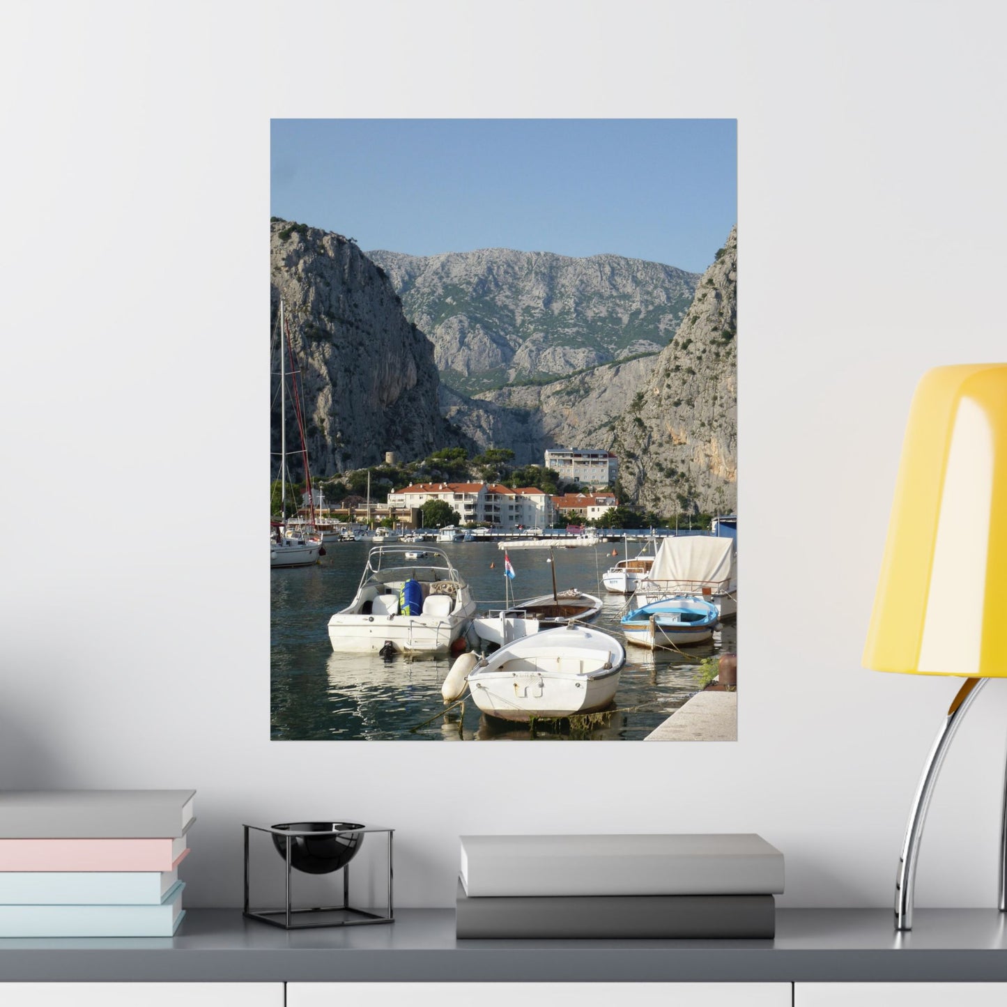 Canvas print of a mountainous coastal scene with boats on a white wall above a shelf.