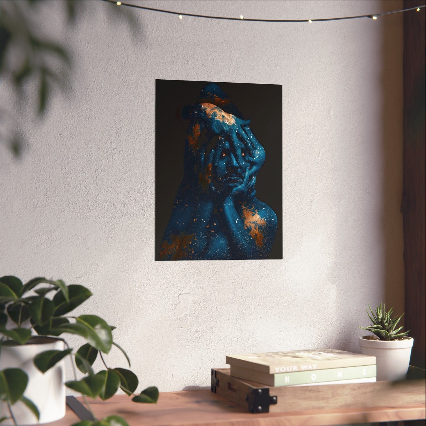 Abstract painting of a face on a wall above a wooden table with books and plants.