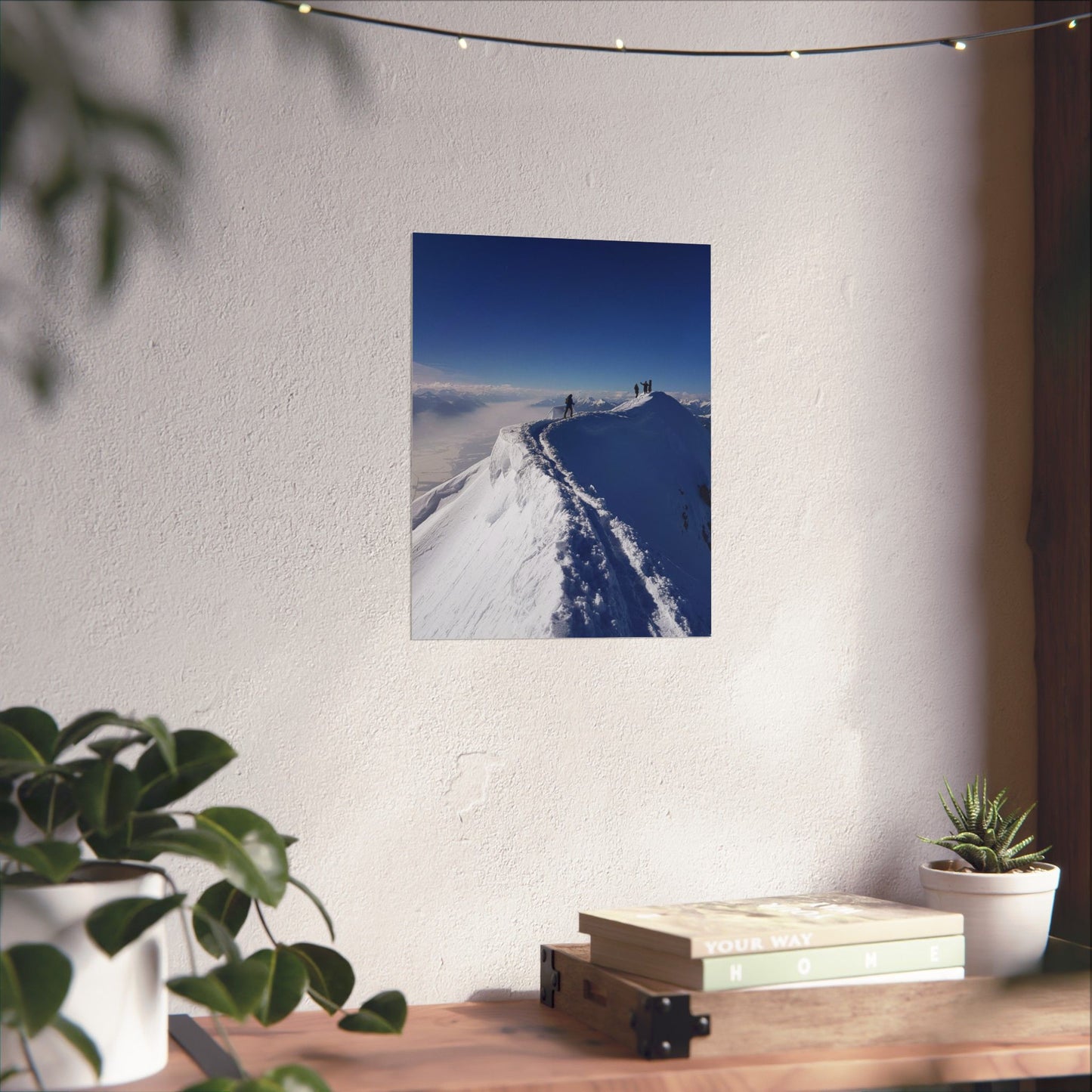Poster of a snowy landscape on a wall above a wooden desk with plants.