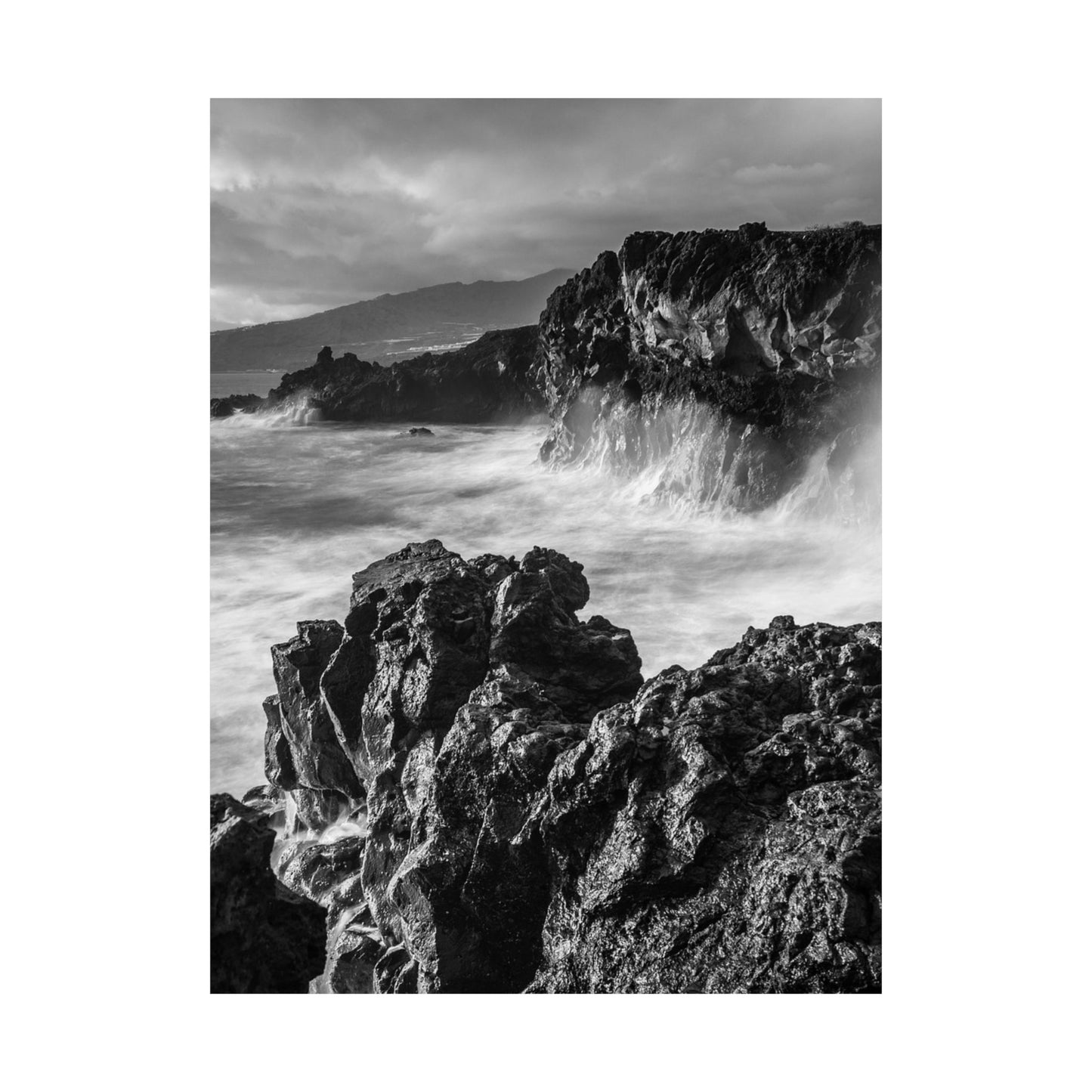 Black and white photograph of rocky coastline with waves crashing against the shore.