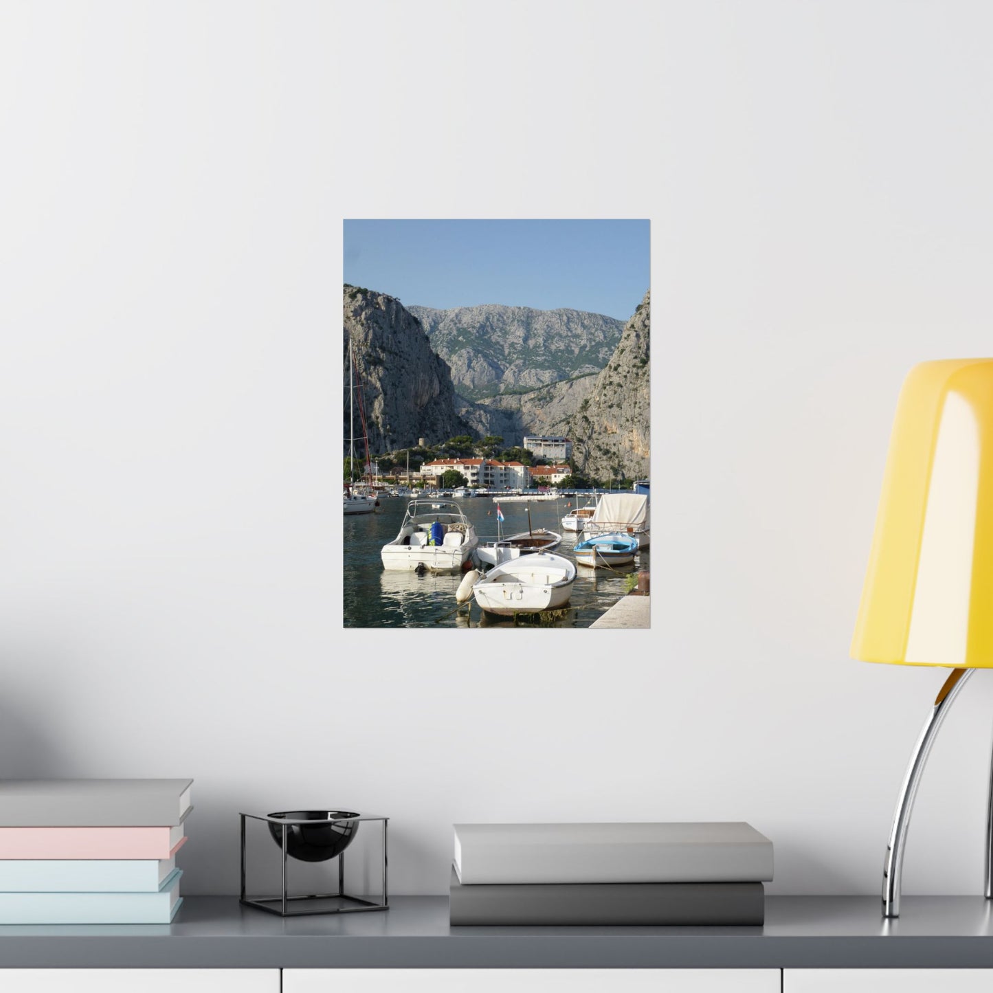 Framed photograph of a coastal scene with boats and mountains on a wall above a desk.