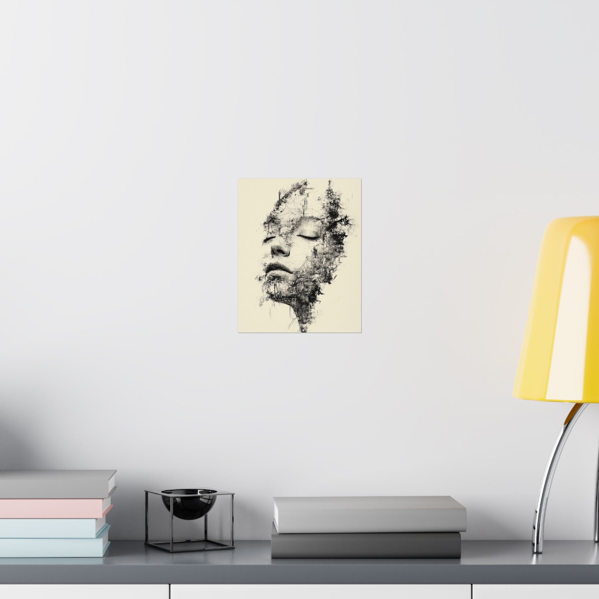 Abstract art print of a face on a wall above a desk with books and a lamp.