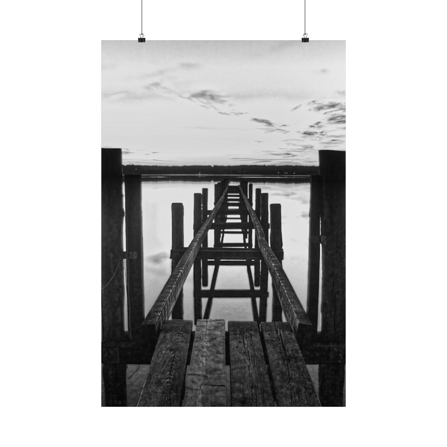 Black and white photo of a wooden pier extending into water with a cloudy sky.