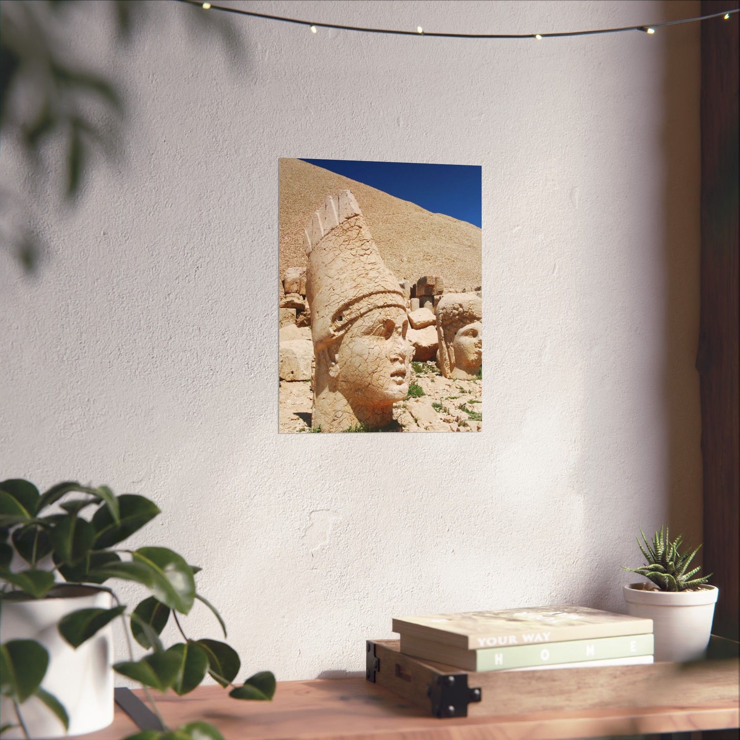 Framed picture of an ancient stone sculpture on a wall above a wooden desk with plants.