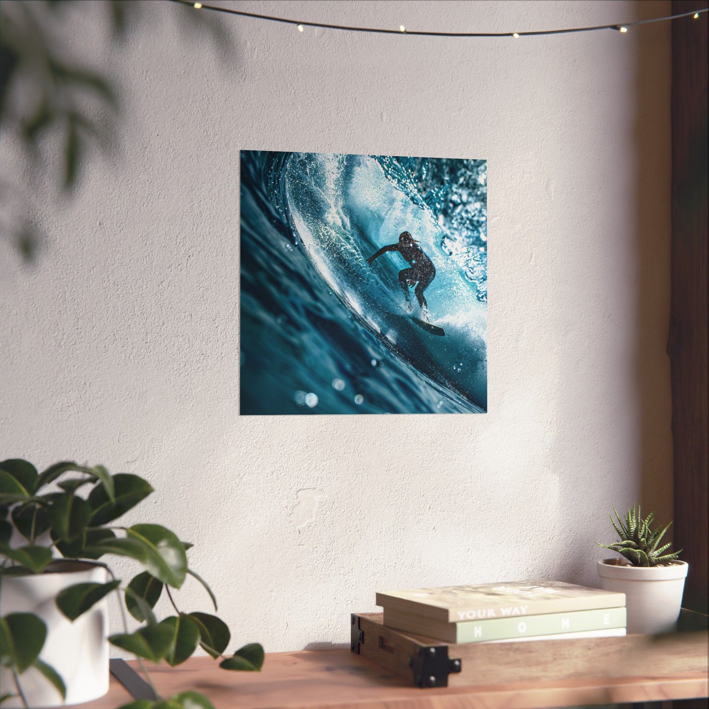 Framed artwork of a surfer on a wave hanging on a wall above a desk with plants.