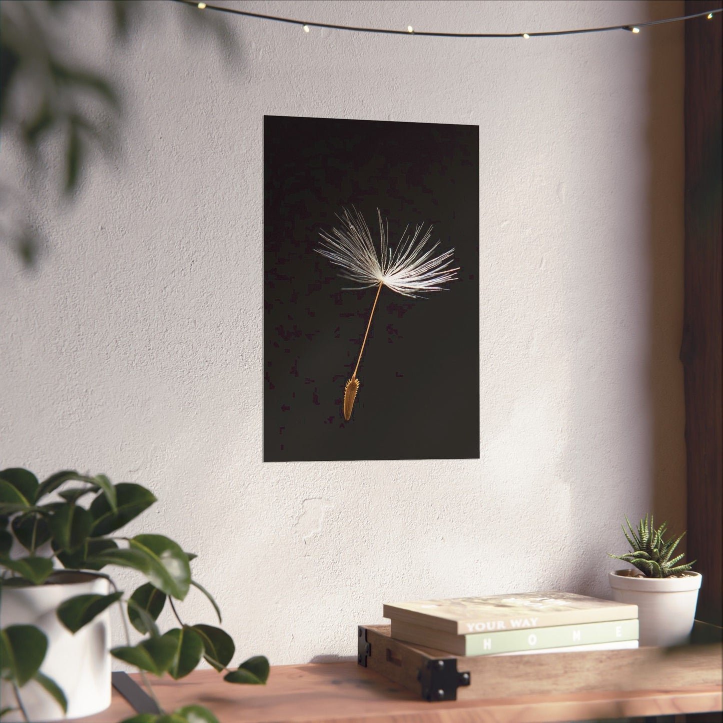 Framed artwork of a dandelion seed head on a wall above a wooden table with plants.