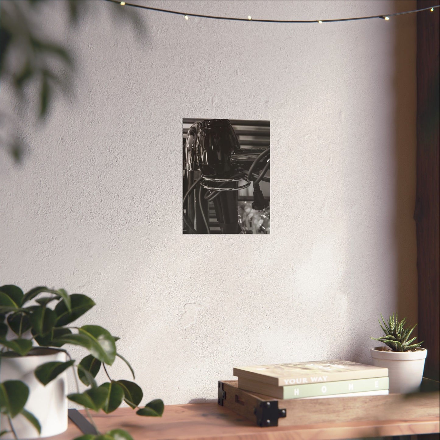 Black and white photo of a bookshelf on a white wall with plants and books on a wooden surface.