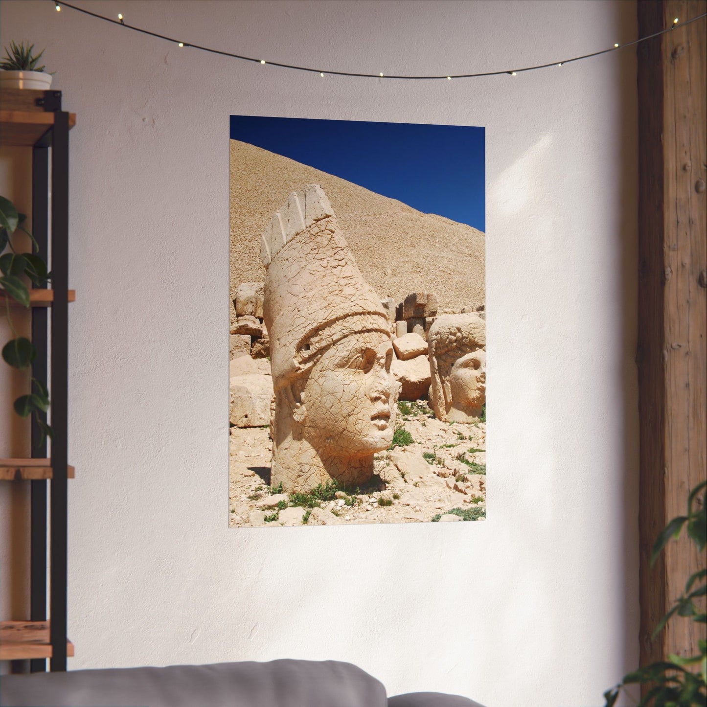 Tapestry with stone heads of ancient statues on a wall, with a shelf and plants in the background.