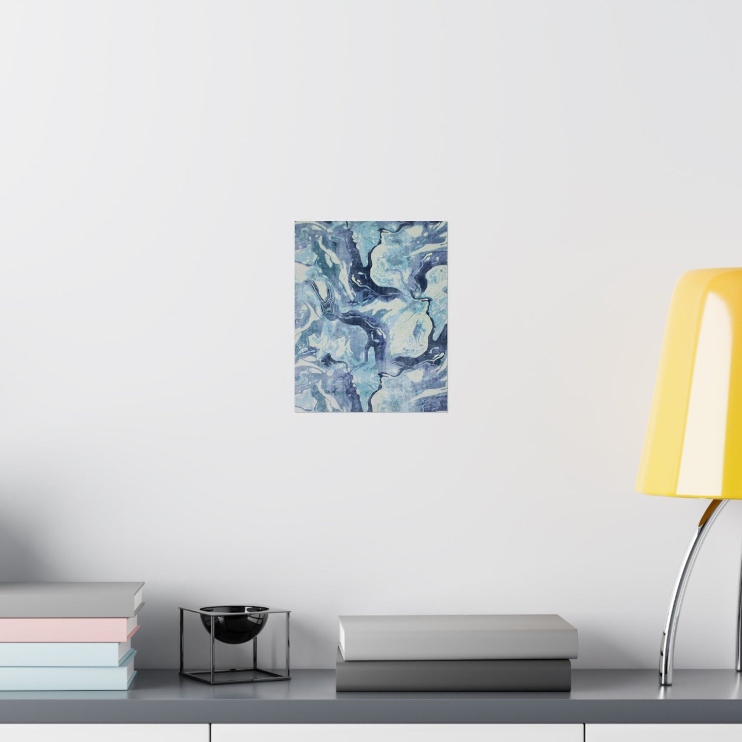 Abstract blue painting on a white wall above a shelf with books and a lamp.