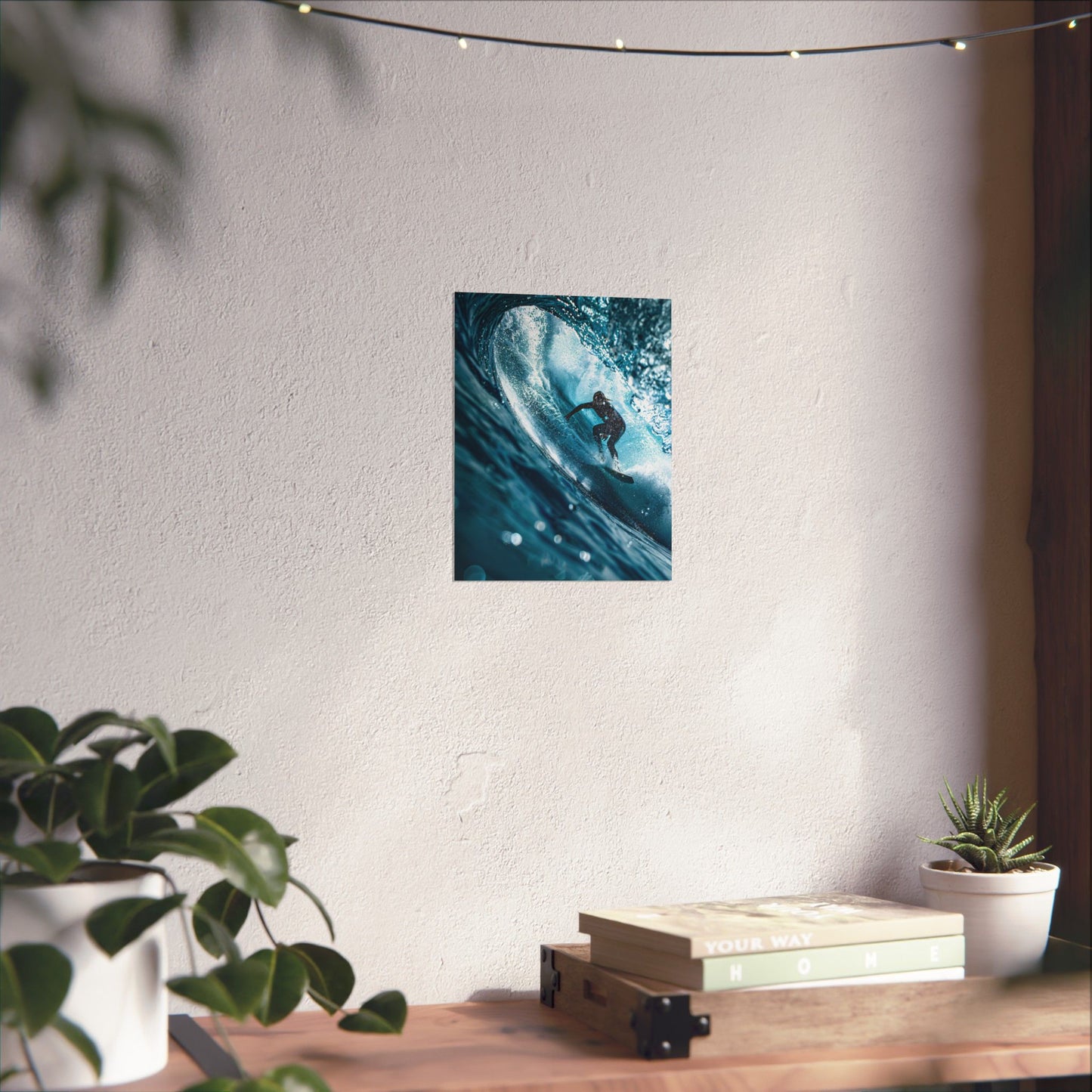 Poster of a surfer in a wave on a white wall above a wooden desk with plants and books.