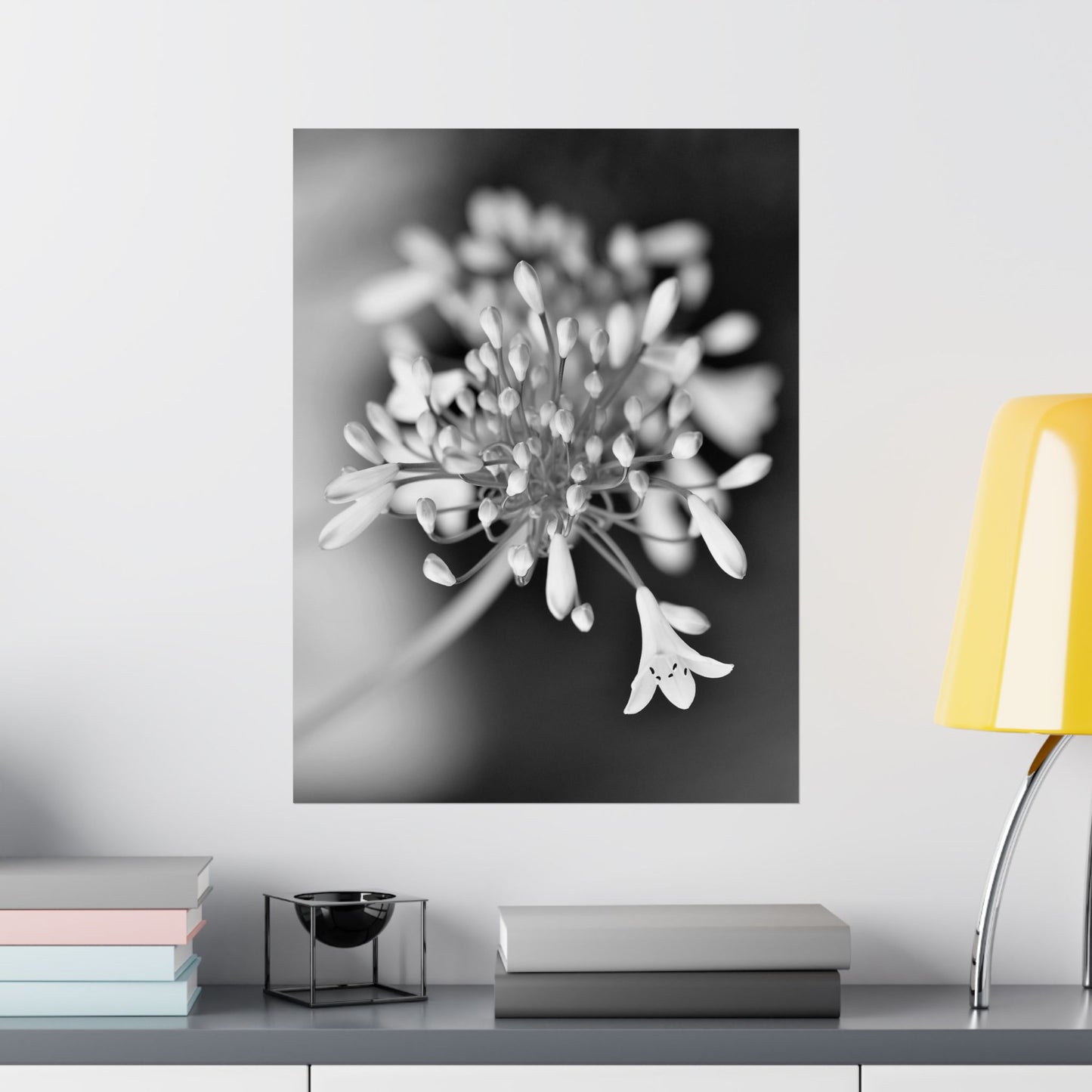 Floral artwork on a wall above a shelf with books and a lamp.