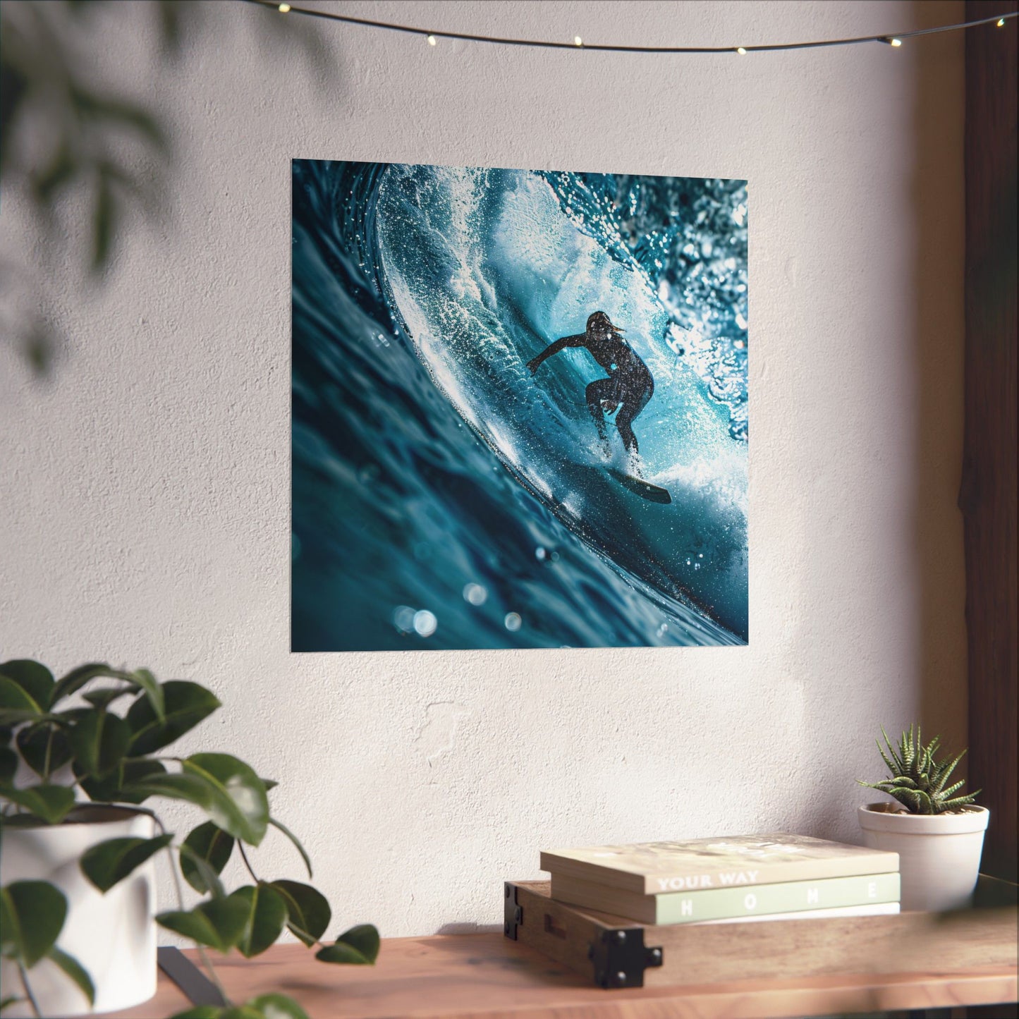 Poster of a surfer on a wave hanging on a wall above a desk with plants.