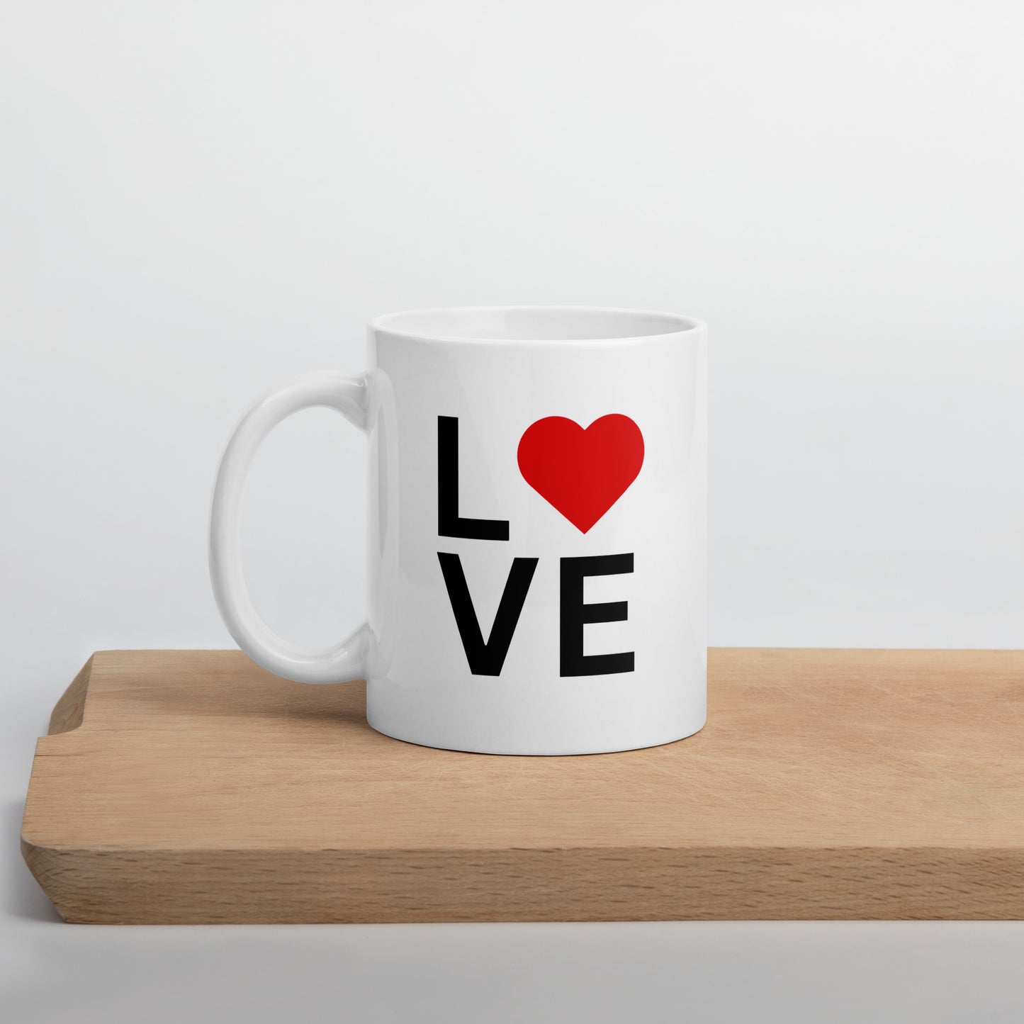 A white ceramic mug with a glossy finish, featuring the text 'love' and a red heart symbol on the front, placed on a wooden board.
