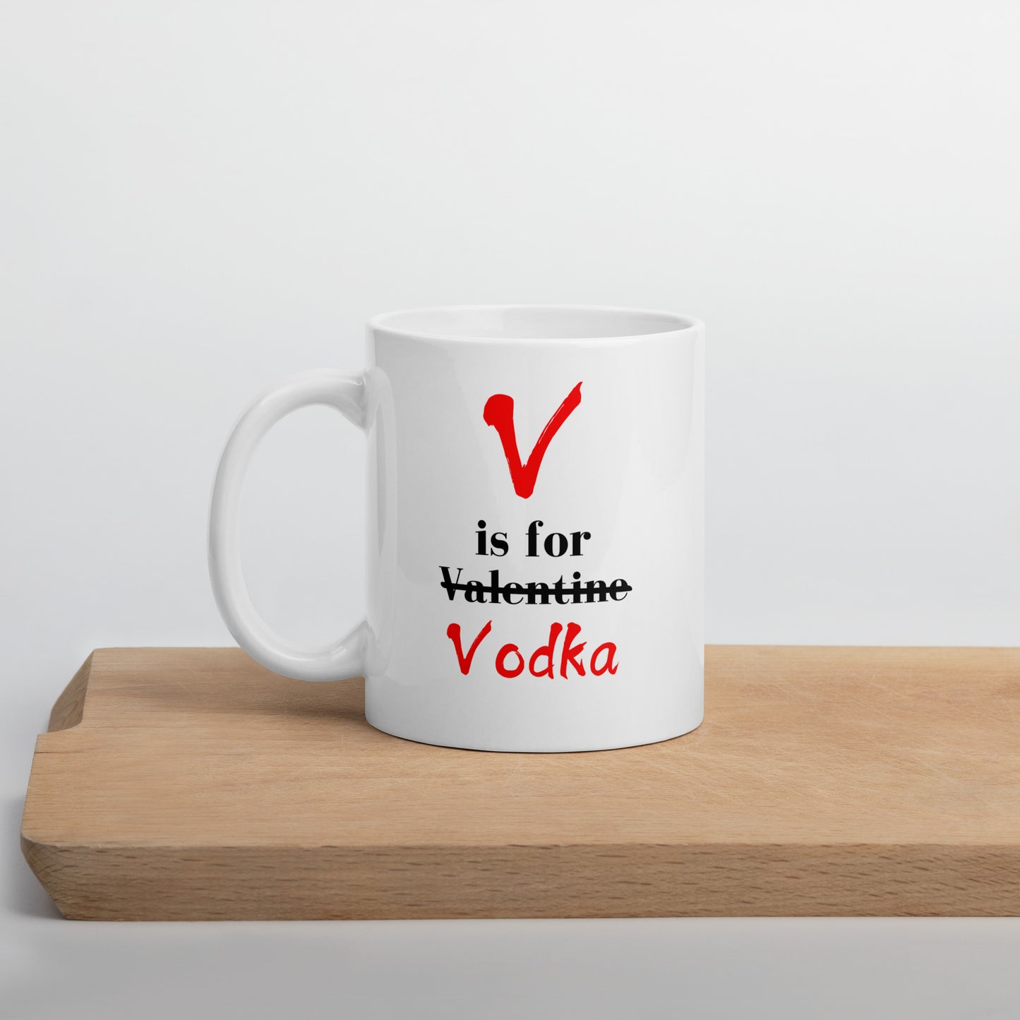 A white ceramic mug with 'V Is For Valentine Vodka' text and a red heart symbol, placed on a wooden board.