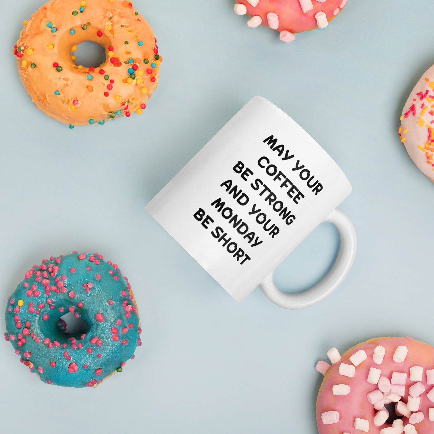 A white ceramic coffee mug with black text reading 'MAY YOUR COFFEE BE STRONG AND YOUR MONDAY BE SHORT'