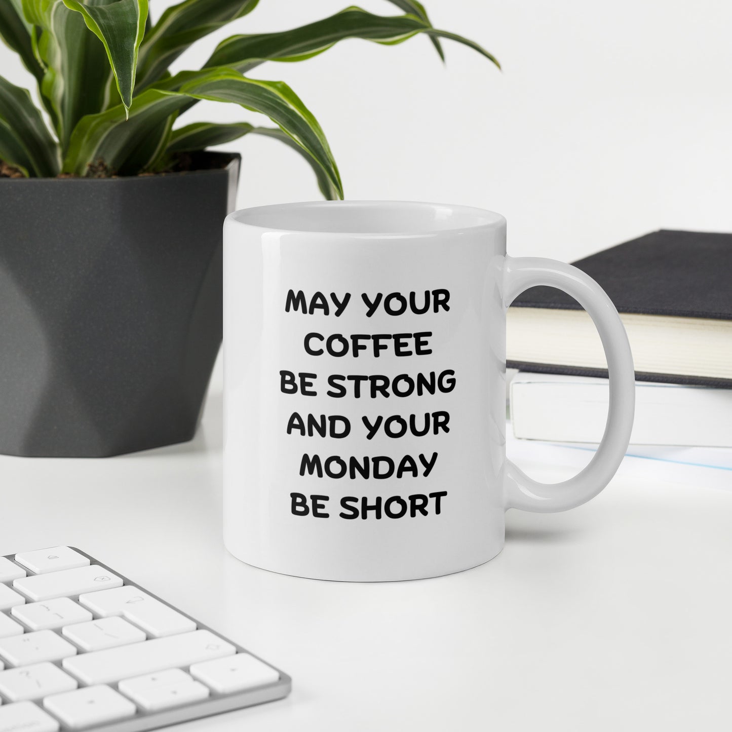 A white ceramic coffee mug with black text reading 'MAY YOUR COFFEE BE STRONG AND YOUR MONDAY BE SHORT'