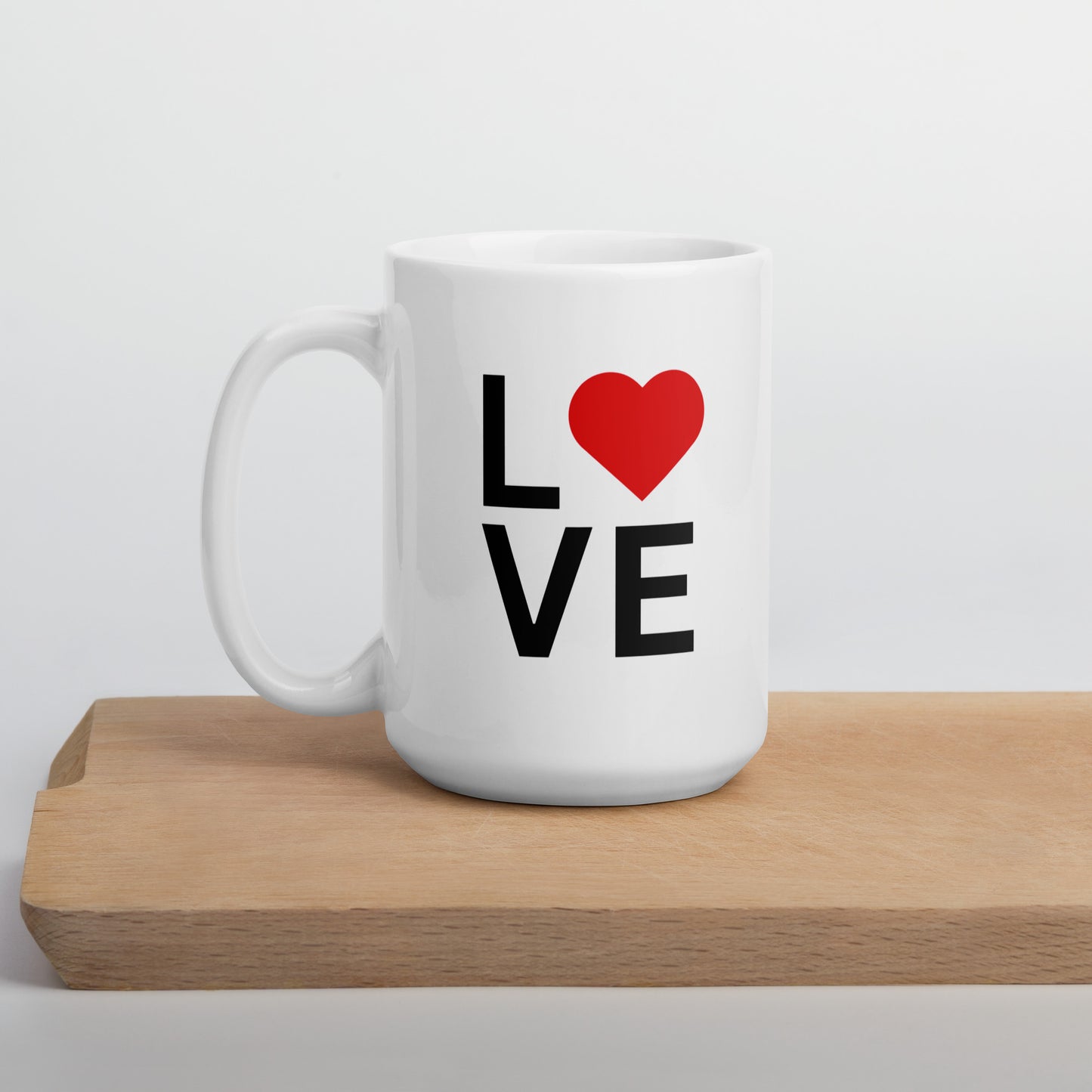 A white ceramic mug with a glossy finish, featuring the text 'love' and a red heart symbol on the front, placed on a wooden board.