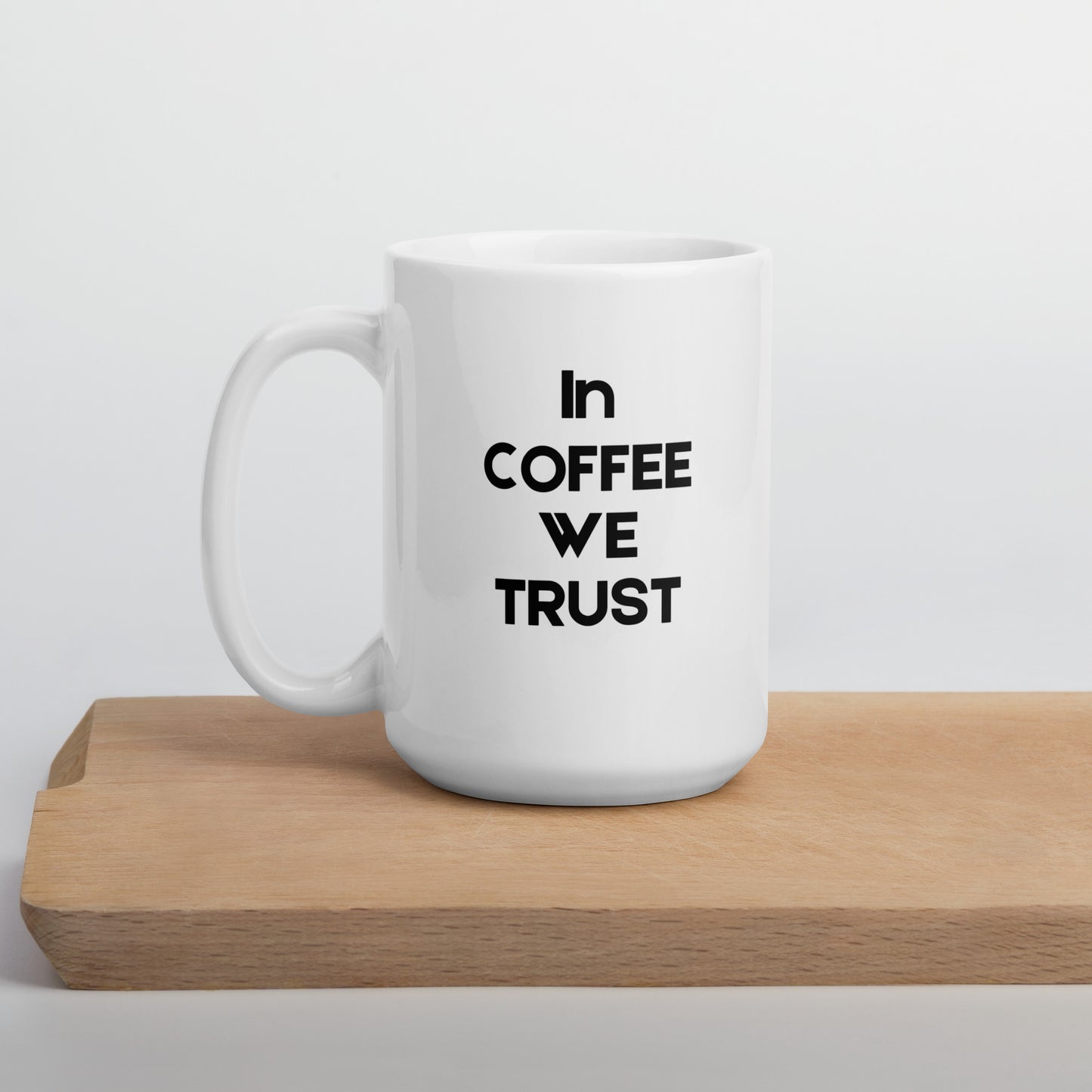 A white ceramic mug with the text 'In Coffee We Trust' printed in black on the front, placed on a wooden board.