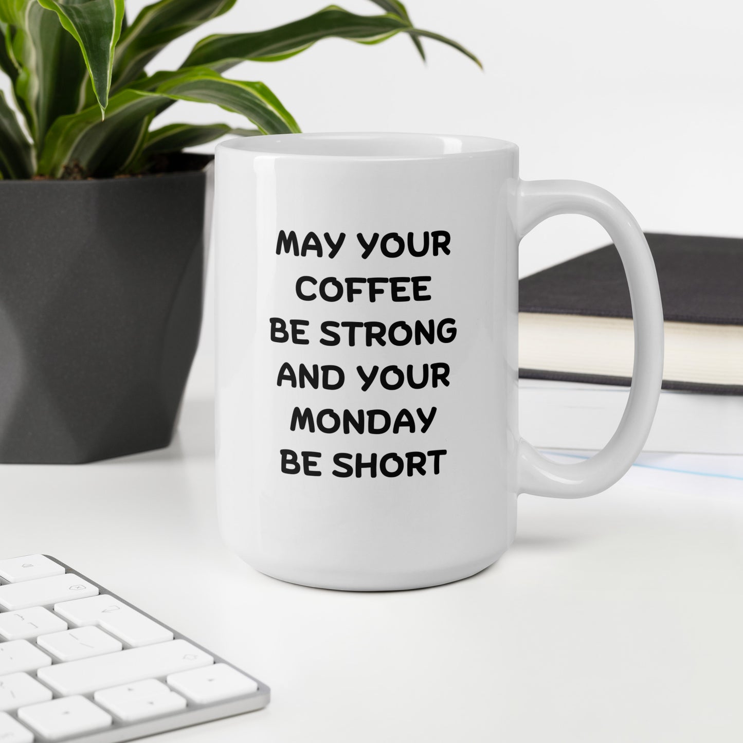 A white ceramic coffee mug with black text reading 'MAY YOUR COFFEE BE STRONG AND YOUR MONDAY BE SHORT'
