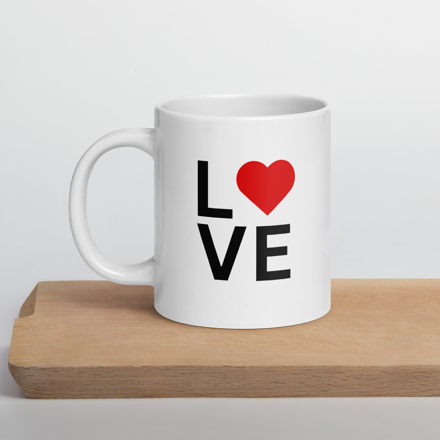 A white ceramic mug with a glossy finish, featuring the text 'love' and a red heart symbol on the front, placed on a wooden board.