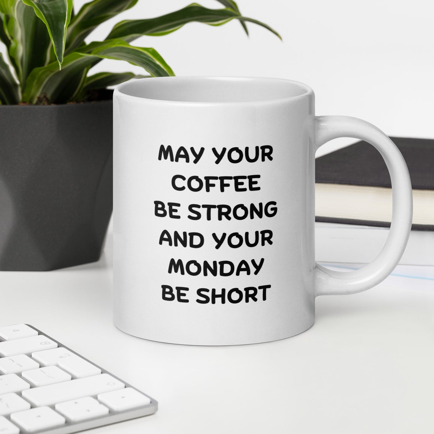 A white ceramic coffee mug with black text reading 'MAY YOUR COFFEE BE STRONG AND YOUR MONDAY BE SHORT'