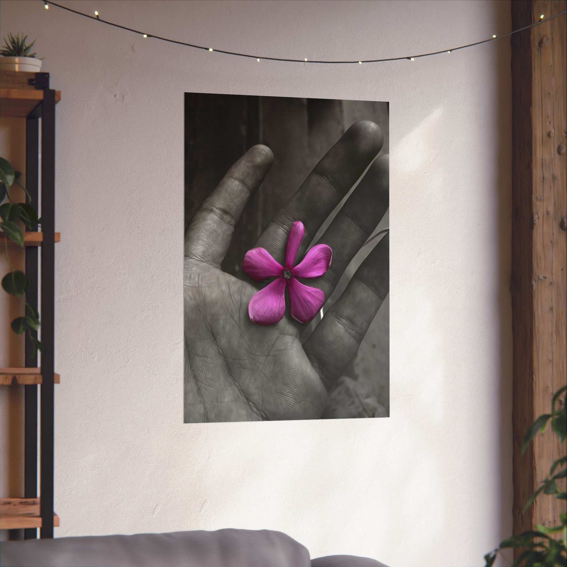 Poster of a hand holding a pink flower on a wall with decorative lights and plants.
