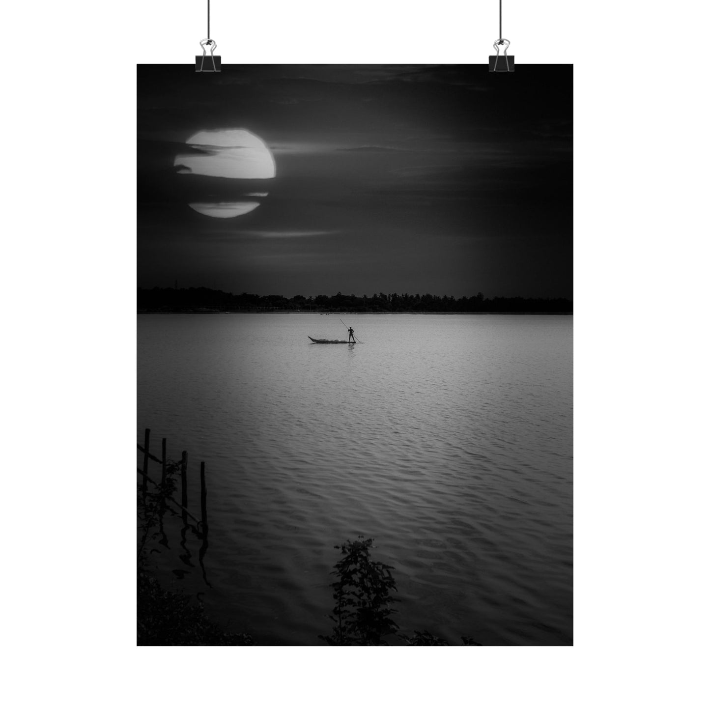Black and white photo of a person in a boat on a lake with a large moon in the sky.