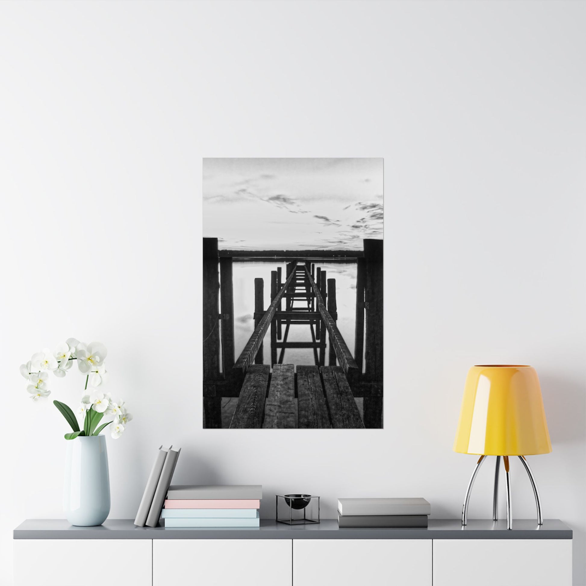 Framed black and white artwork of a dock on a wall above a shelf with decor items.