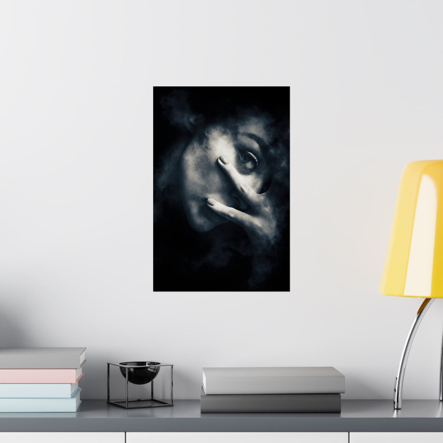 Framed artwork of a face on a wall above a desk with books and a lamp.