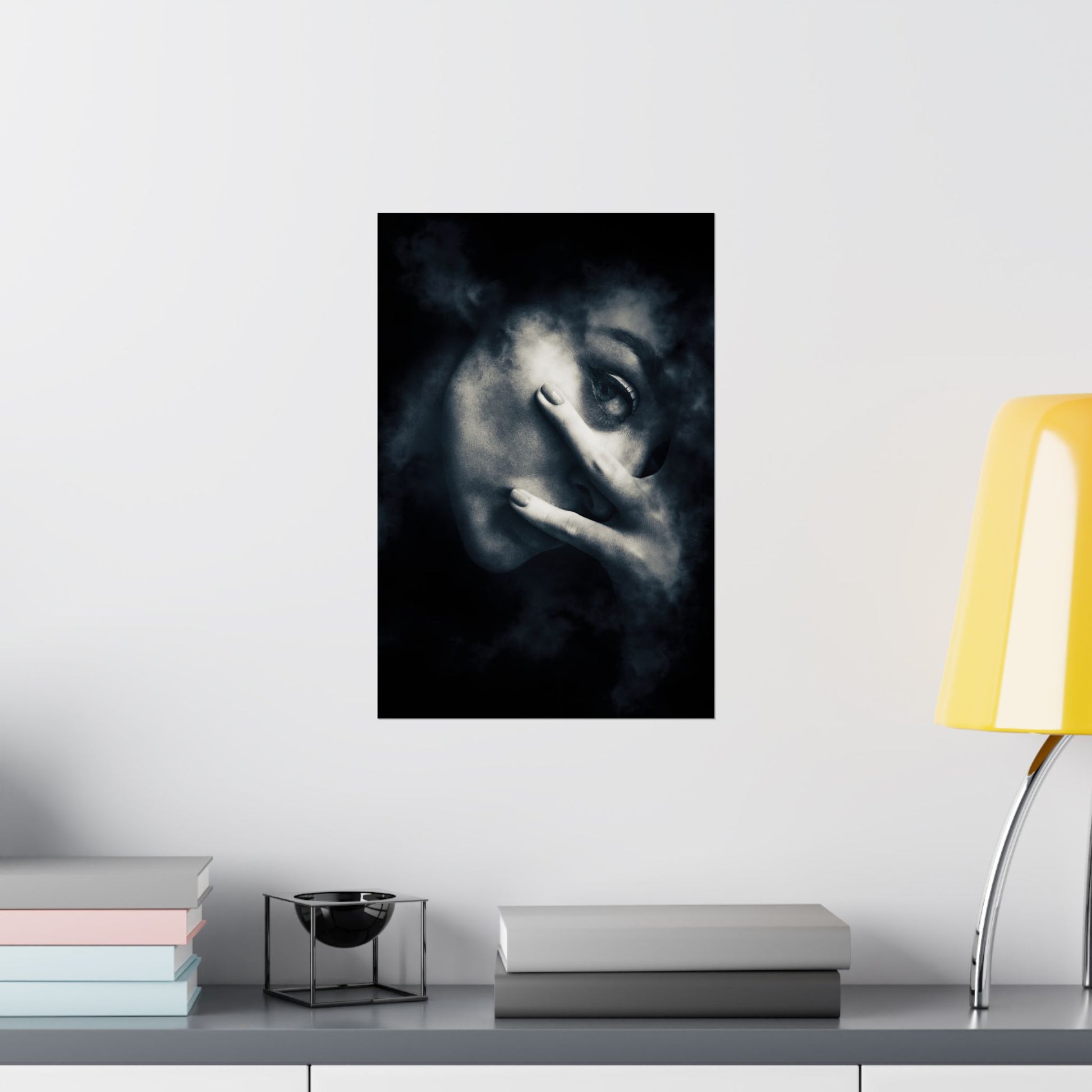 Framed artwork of a face on a wall above a desk with books and a lamp.