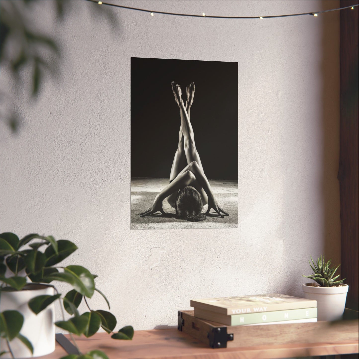 Poster of a yoga pose on a wall with plants and books on a table below.