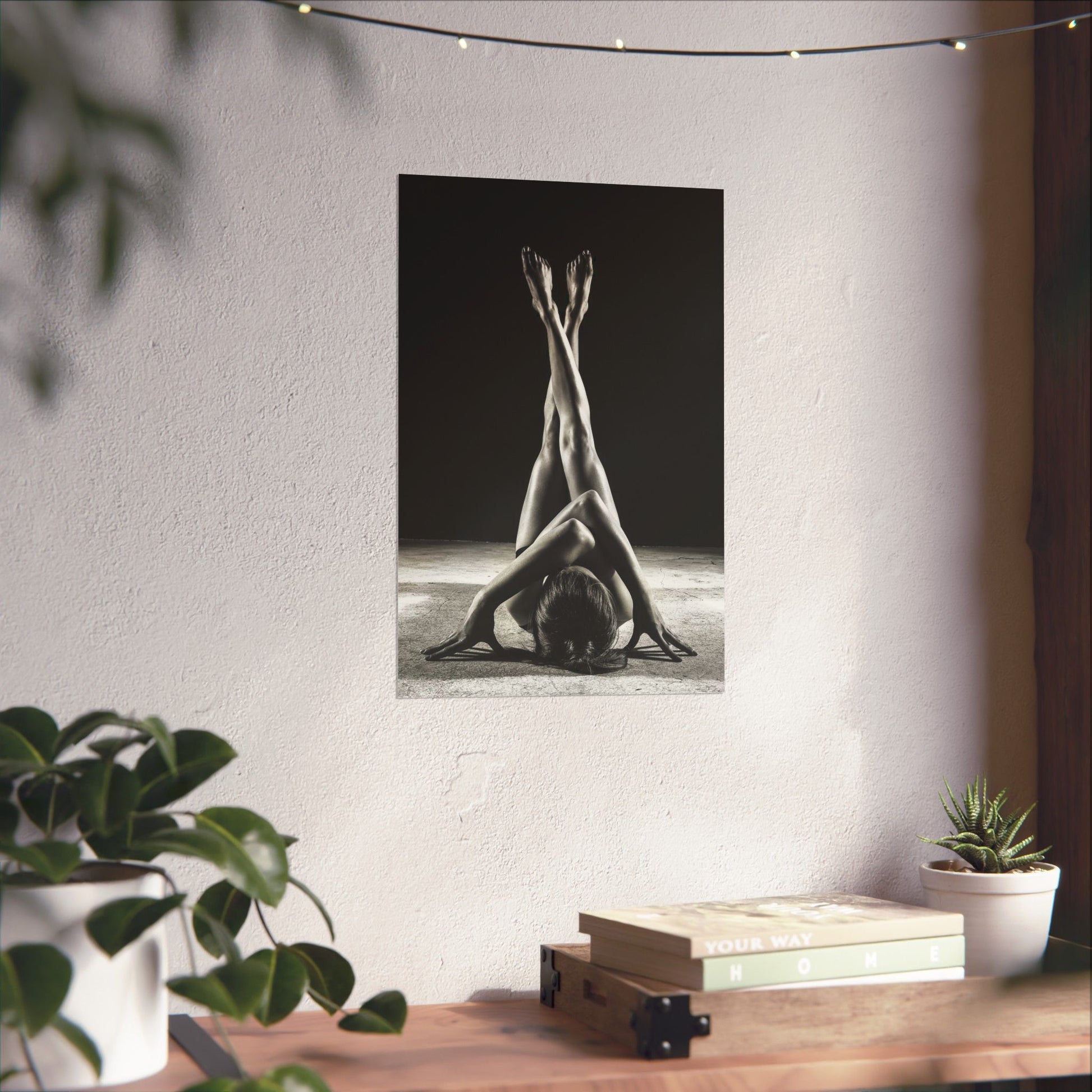 Poster of a yoga pose on a wall with plants and books on a table below.