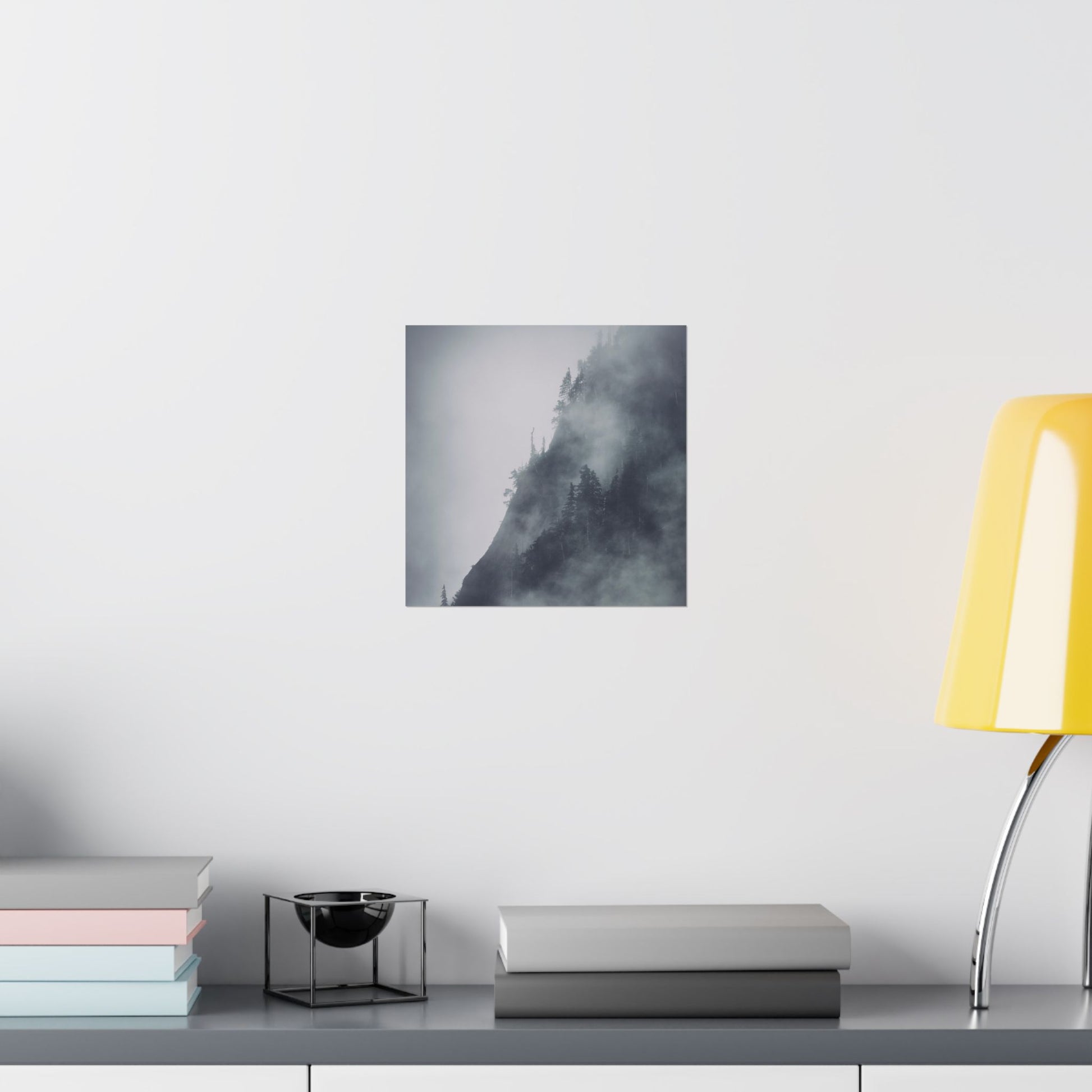 Art print of a mountain landscape on a wall above a desk with books and a lamp.