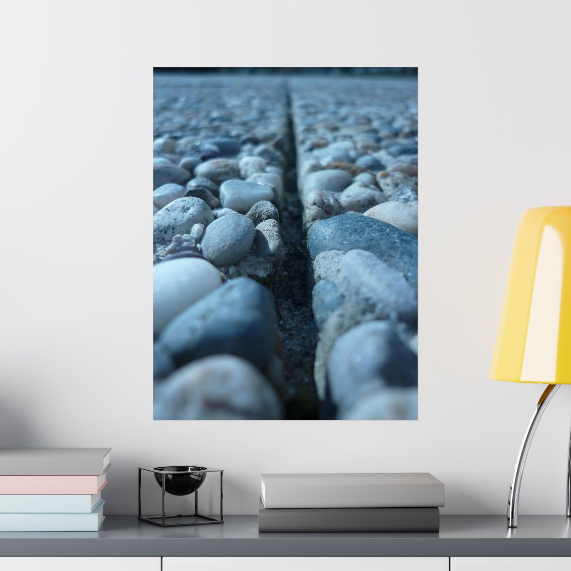 Wall art of pebbles on a white wall with a yellow lamp and books below.