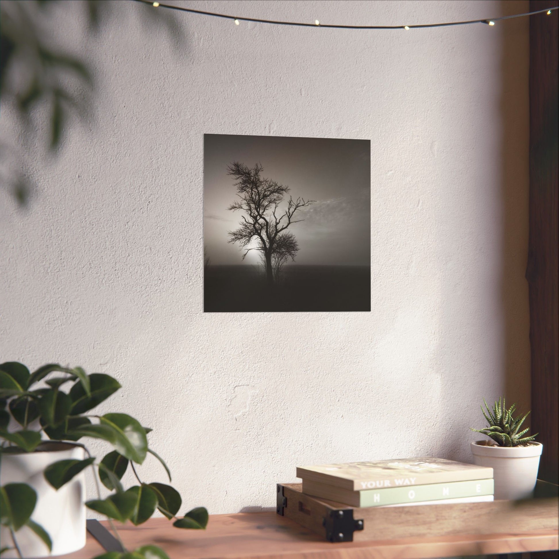 Framed black and white tree print on a wall above a wooden desk with plants.