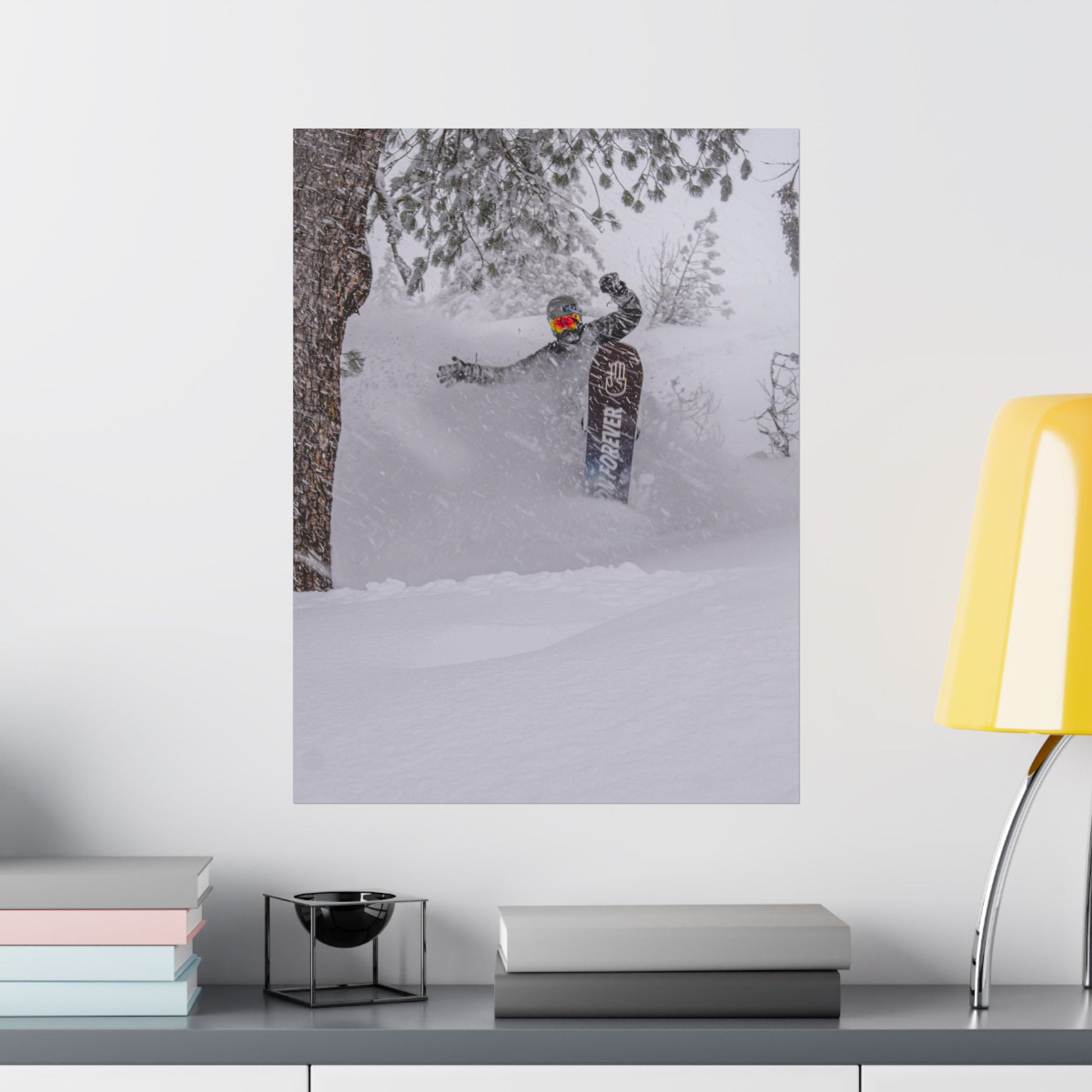 Poster of a person snowboarding on a wall above a desk with books and a lamp.