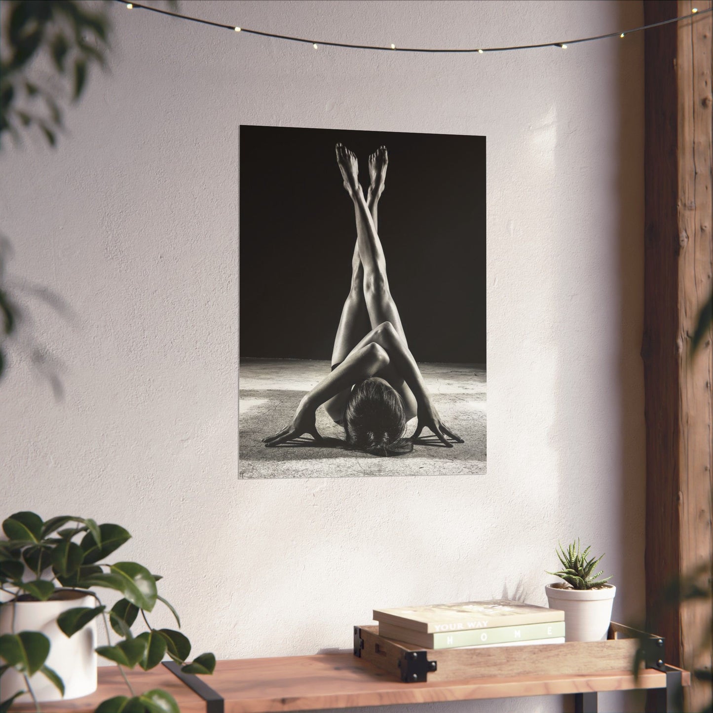 Black and white art print of a person in a yoga pose on a wall with plants and books below.