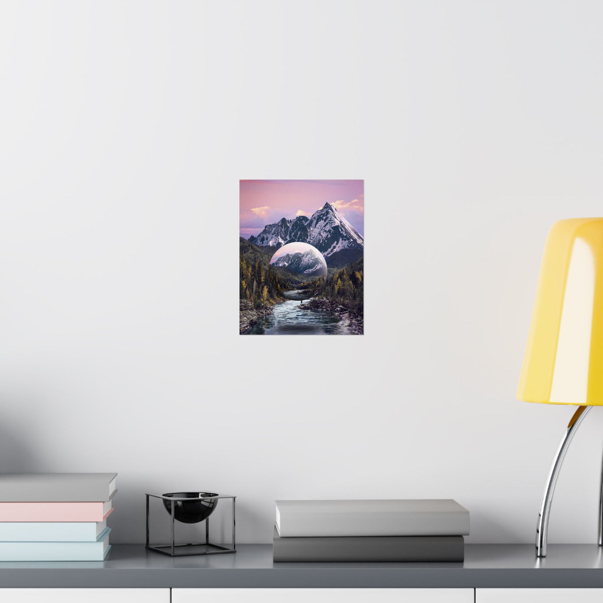 Framed artwork of a mountain landscape with a purple sky on a white wall above a desk.