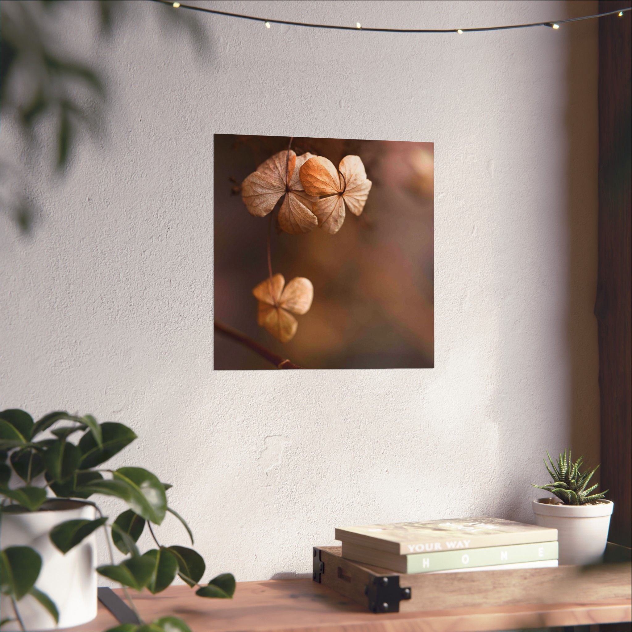 Decorative wall art of dried flowers on a white wall with plants and books below.