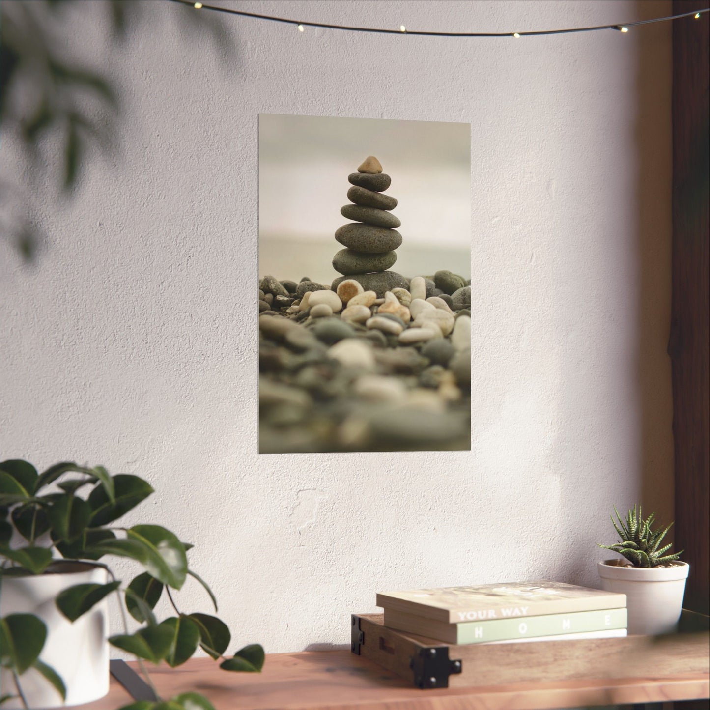 Stack of stones on a white wall with plants and books on a table below.