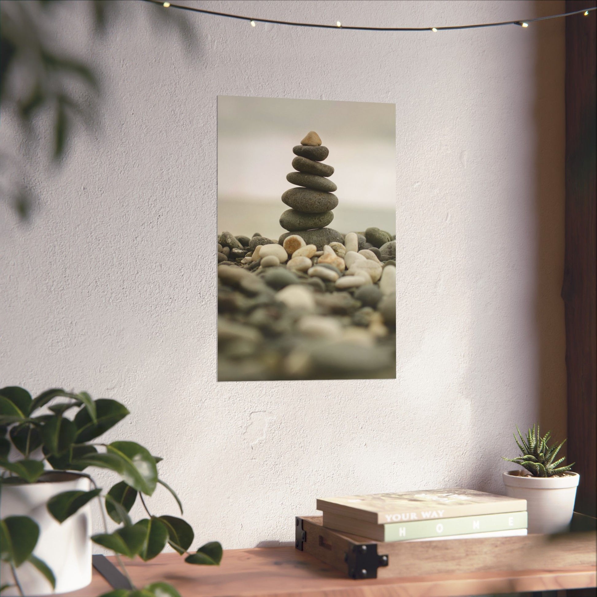 Stack of stones on a white wall with plants and books on a table below.