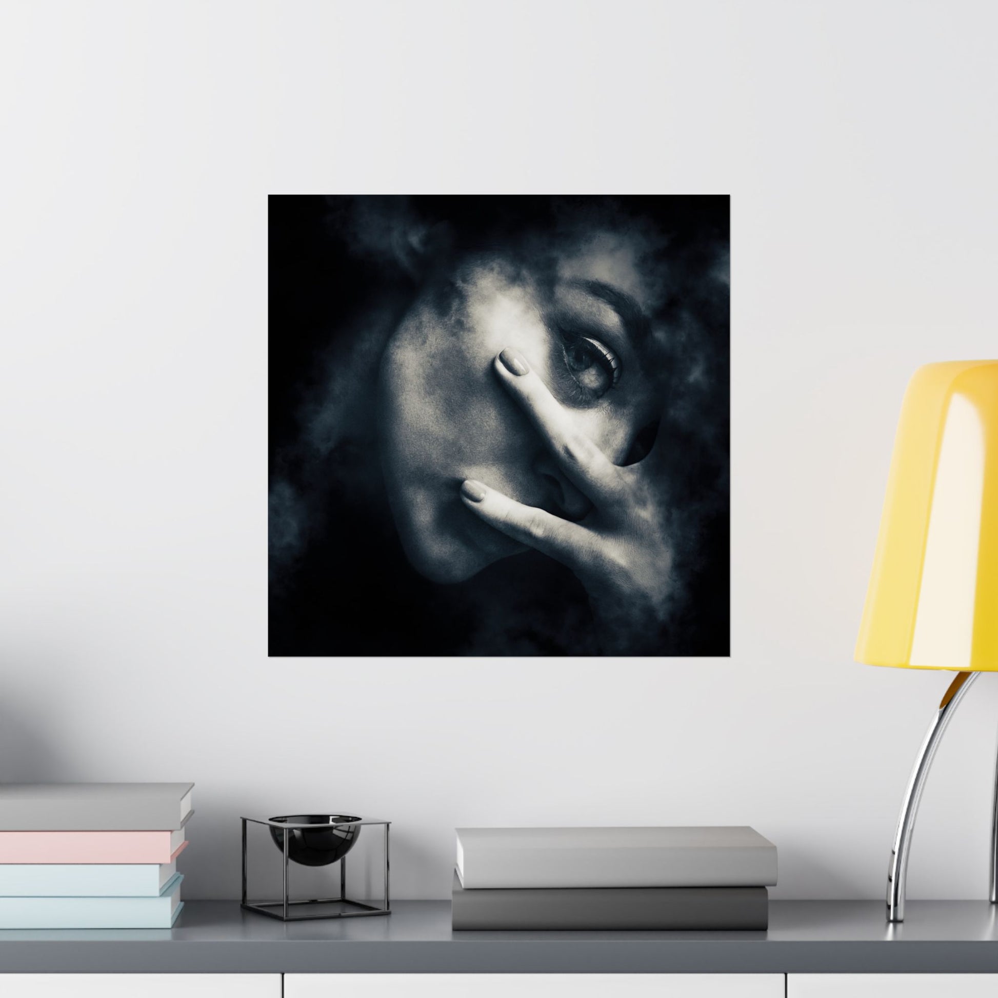 Framed artwork of a stylized face on a wall above a shelf with books and a lamp.