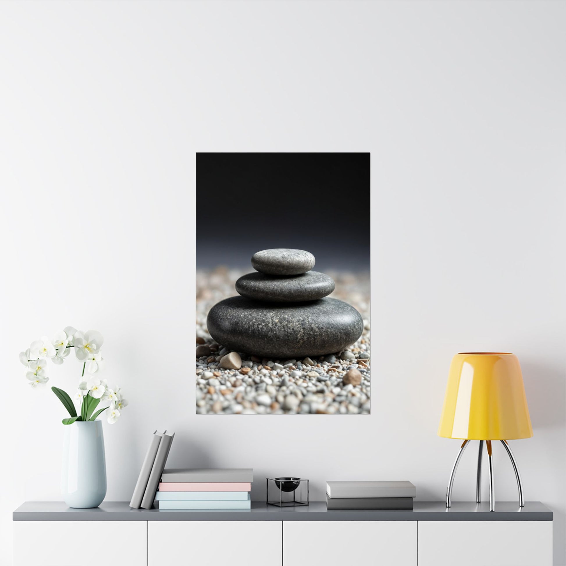 Framed artwork of stacked stones on a wall above a table with decor items.