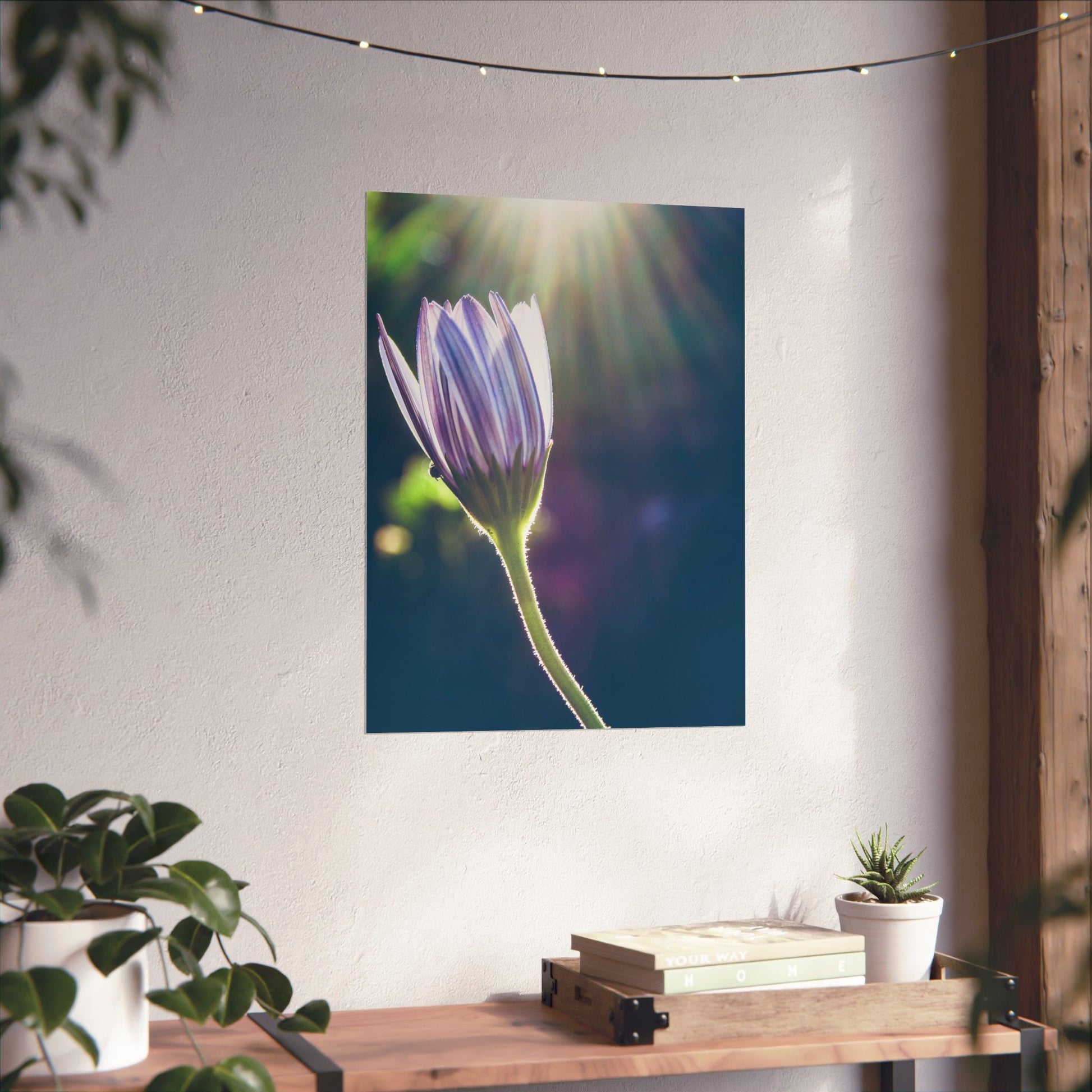 Flower painting on a wall above a wooden table with books and plants.