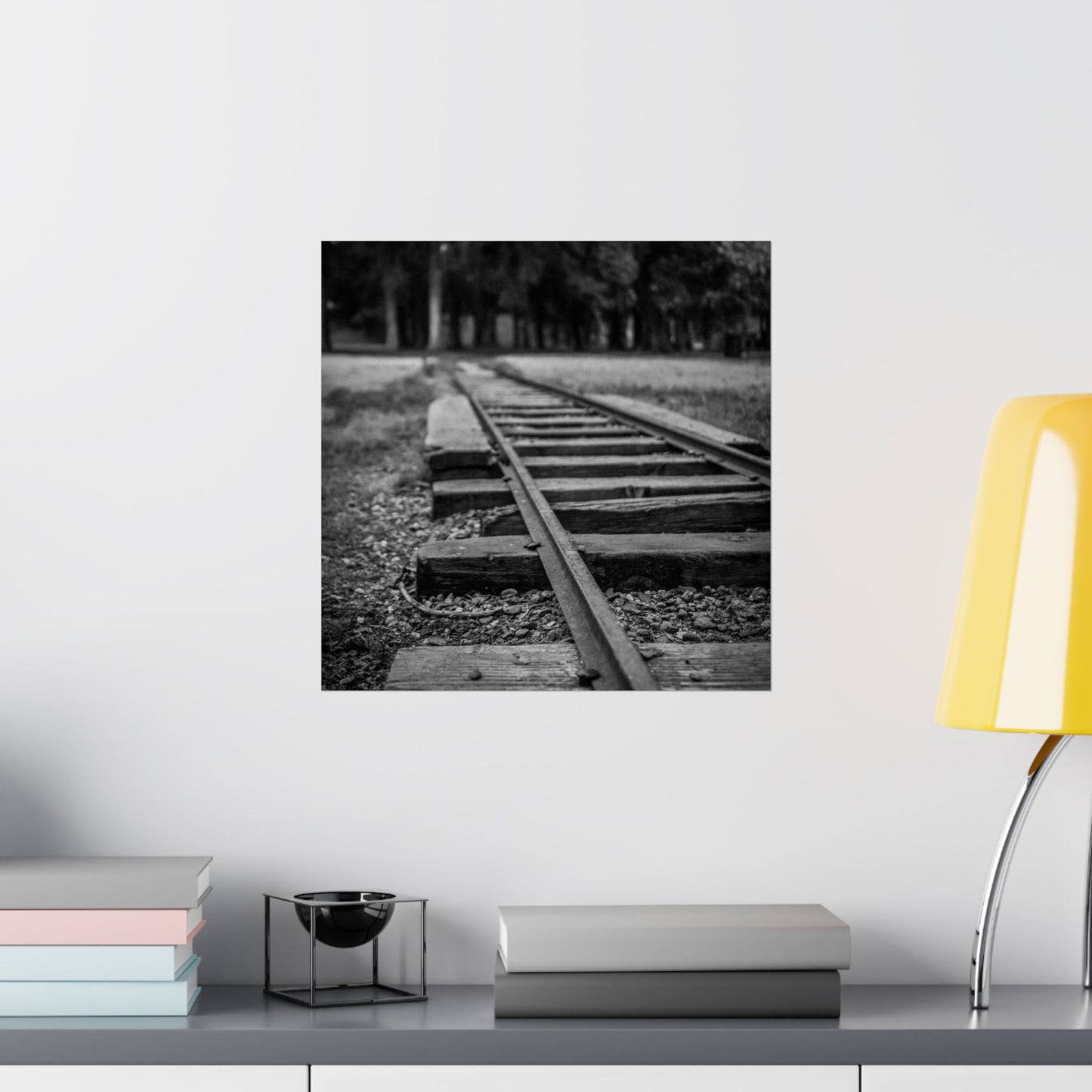 Framed black and white photograph of a railway track on a wall above a shelf with books and a lamp.