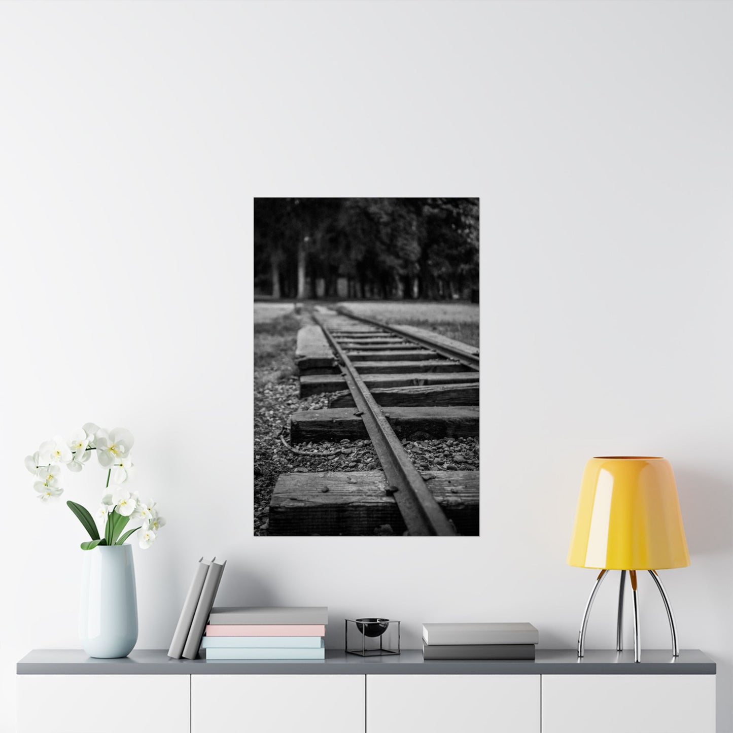 Framed black and white photo of a railway track on a wall above a shelf with decor items.