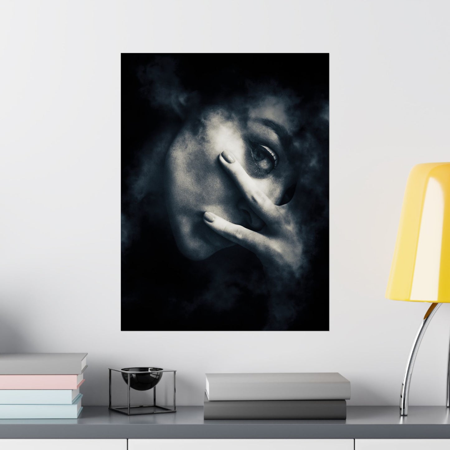 Framed artwork of a face with a hand over one eye on a wall above a shelf.