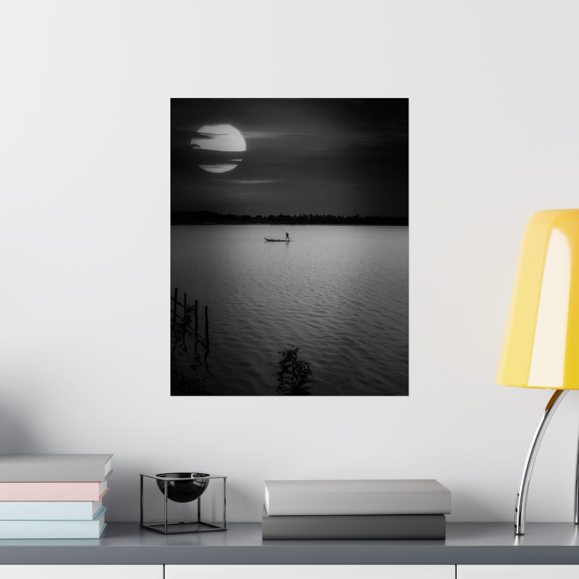 Framed black and white artwork of a sunset over water on a wall above a shelf.
