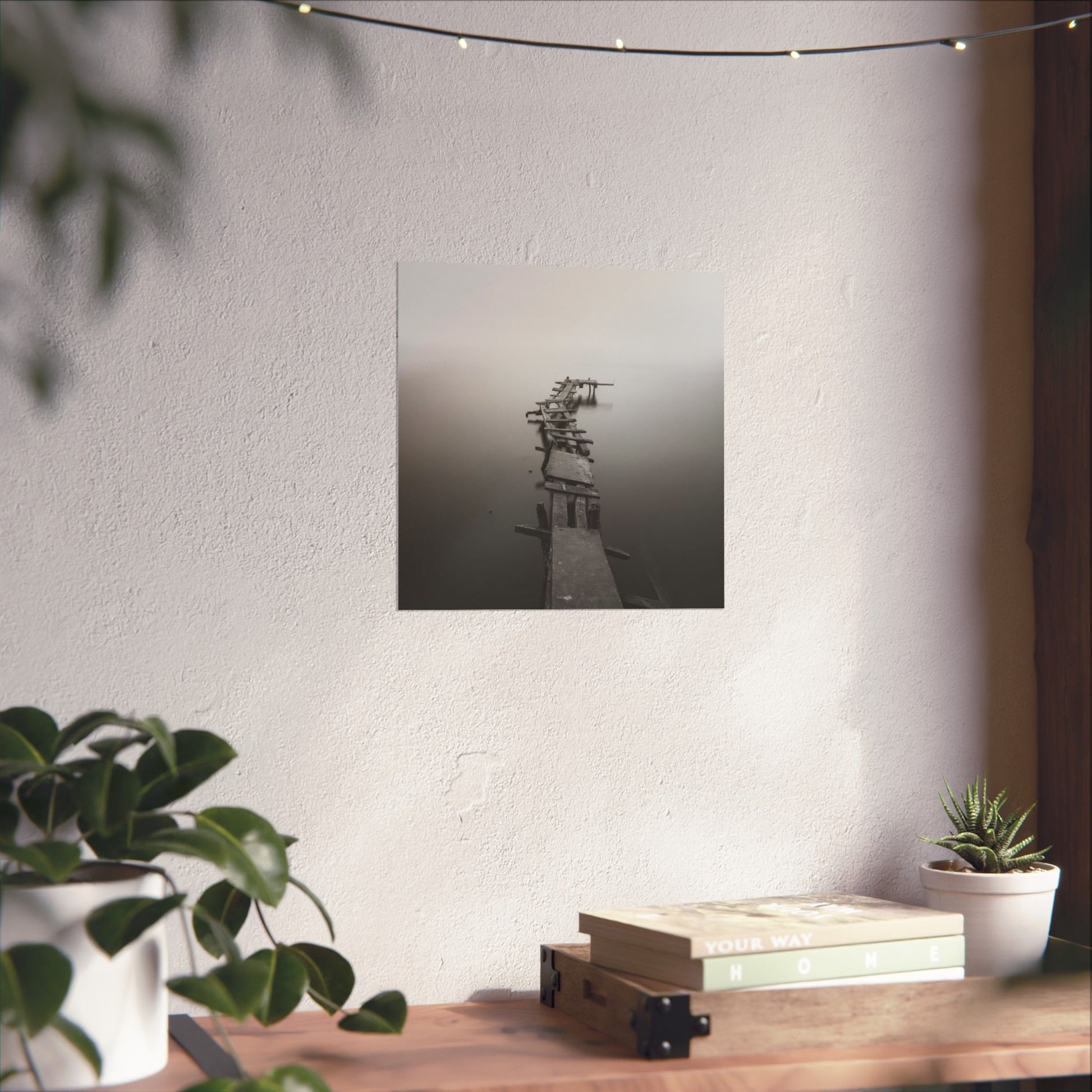 Framed black and white photograph on a wall above a wooden desk with plants and books.