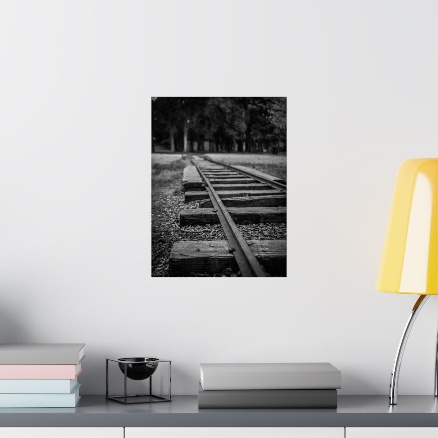 Framed black and white photograph of a railway track on a wall above a shelf with books and a lamp.
